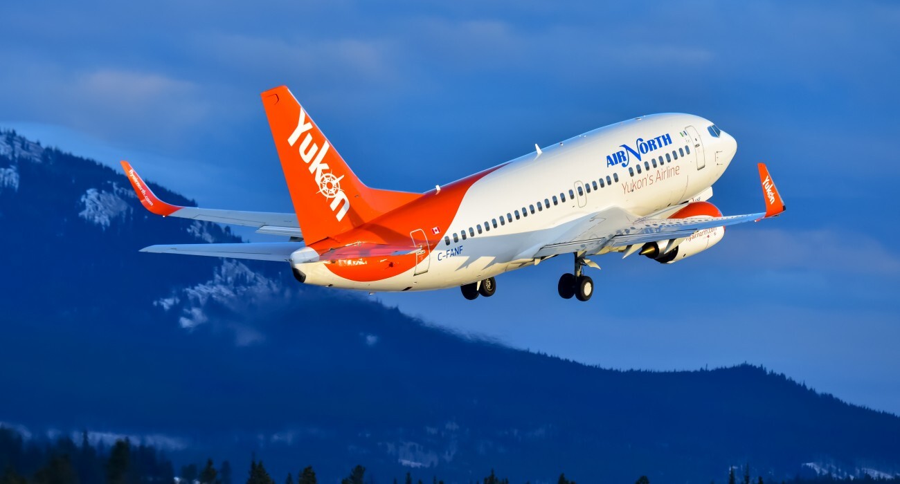 Air North Boeing 737 departing with landing gear extended, flying in front of dark blue mountains.
