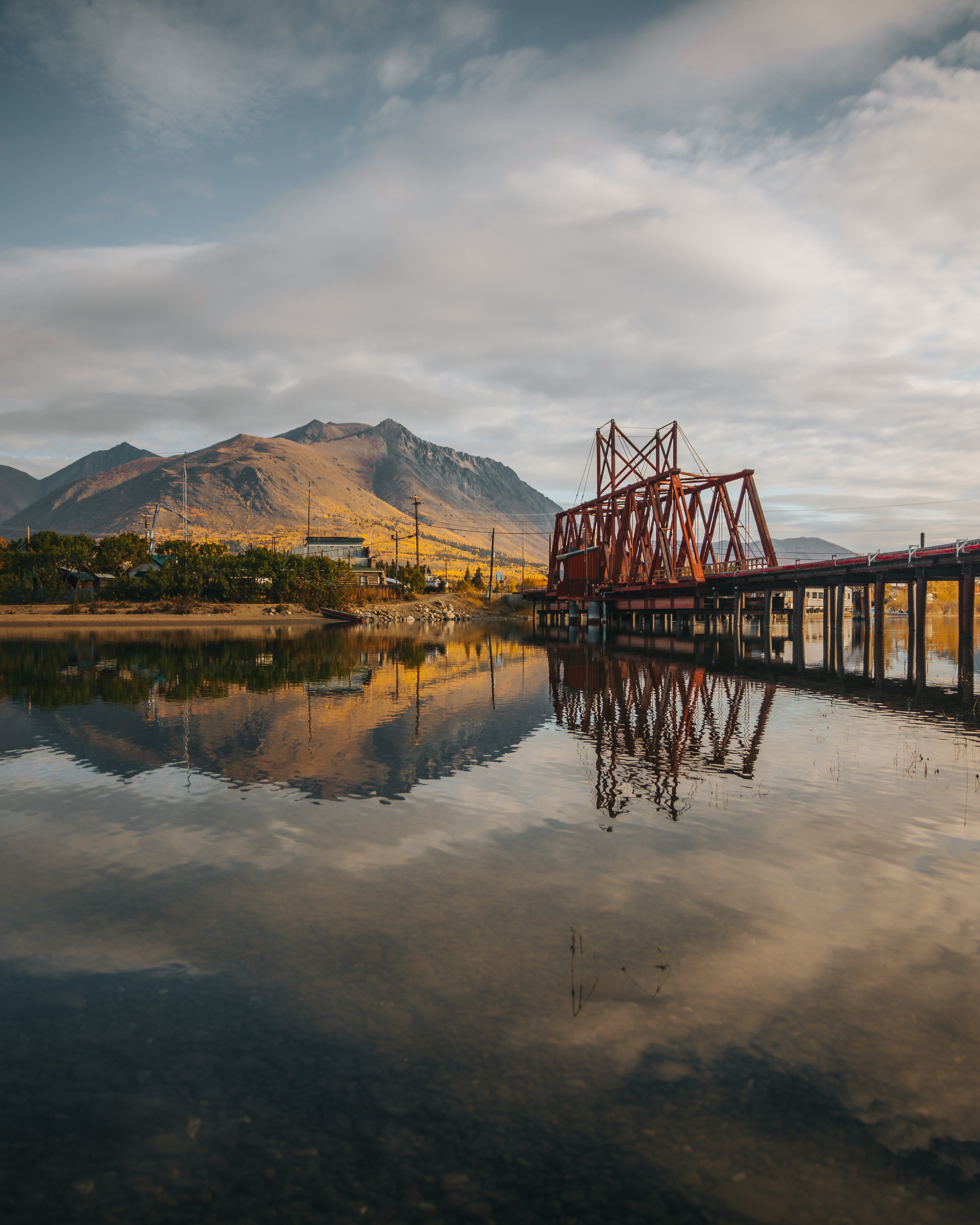 Red railway bridge and mountain reflection in still water at historic Carcross, Yukon, along the Southern Lakes route.