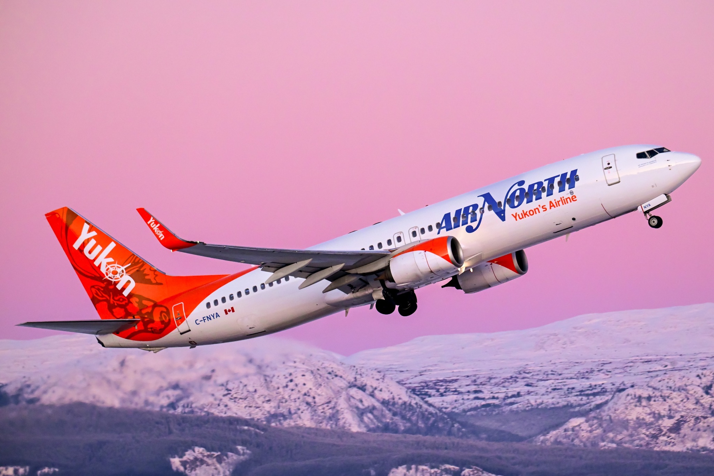 Air North Boeing 737 taking off over a mountain landscape.