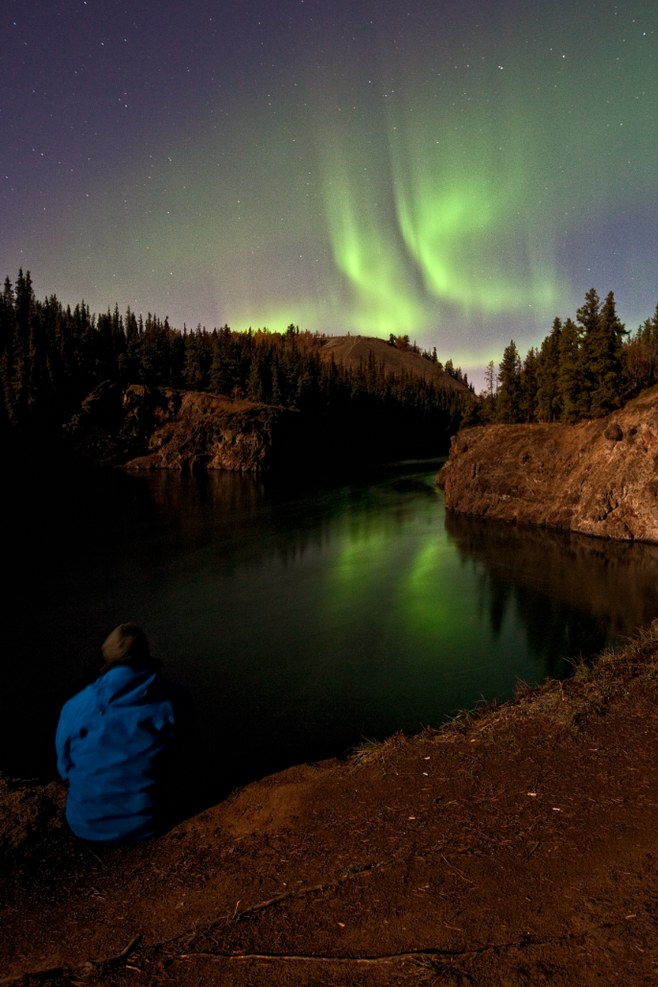Aurora borealis over Miles Canyon near Whitehorse, reflected in still water beneath a northern night sky.