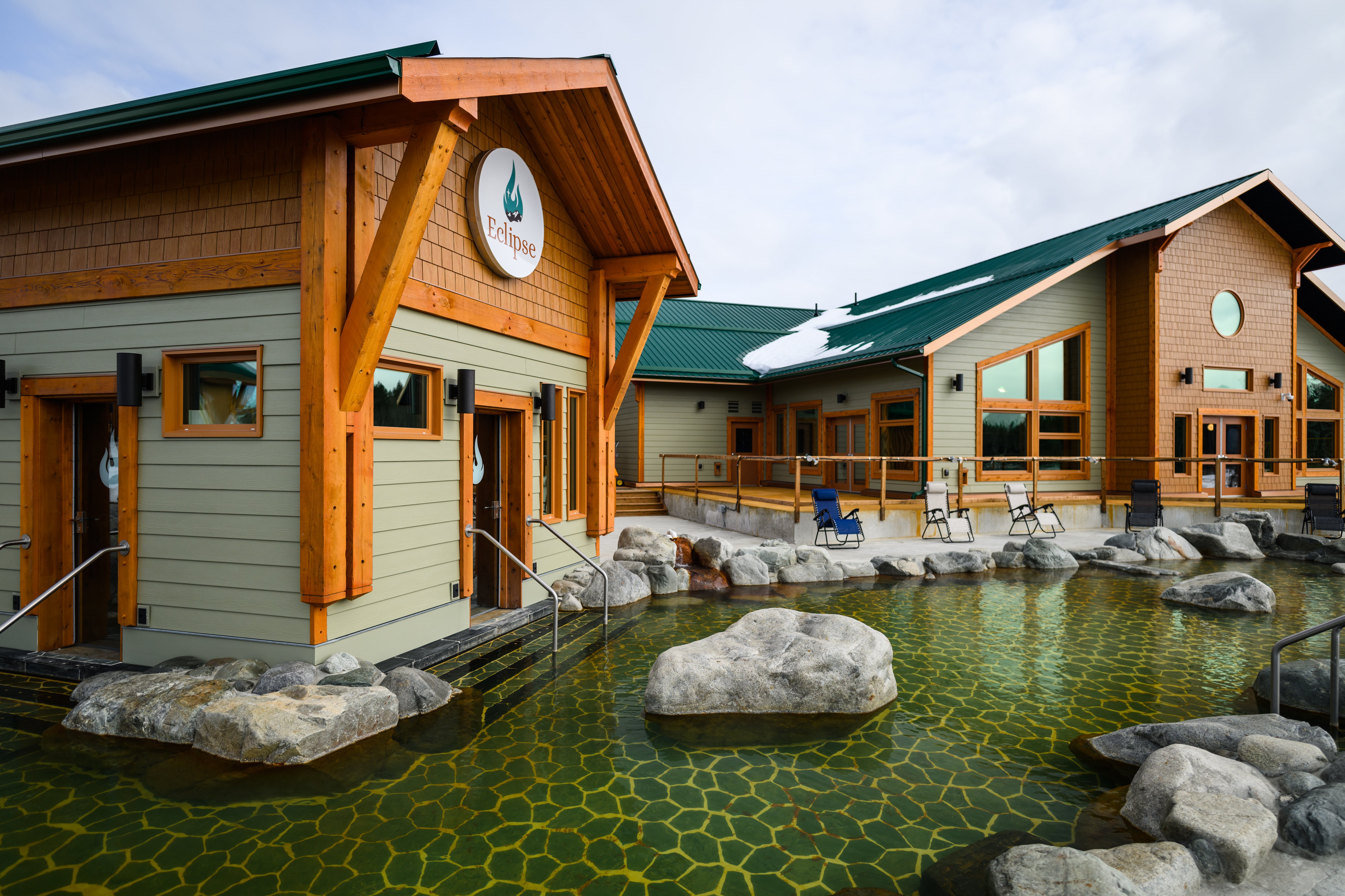 Outdoor thermal pool at Eclipse Nordic Hot Springs near Whitehorse, showing the pool area, surrounding buildings, and forested setting.