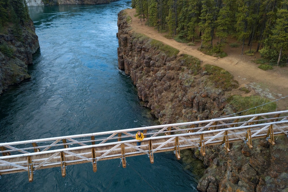 Footbridge over Miles Canyon near Whitehorse, with a traveller crossing above the Yukon River and rocky canyon walls.