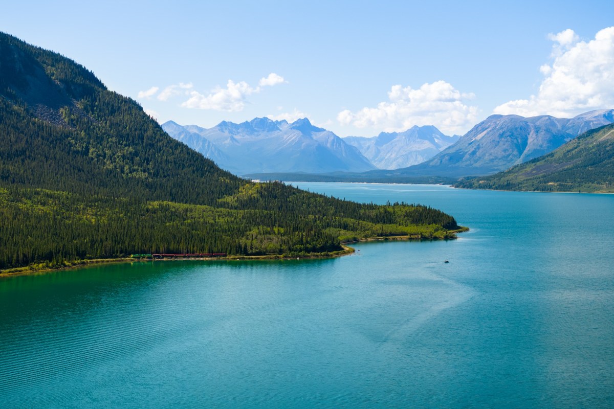 White Pass train travelling beside Bennett Lake, with turquoise water and mountain scenery in the Yukon and northern British Columbia.